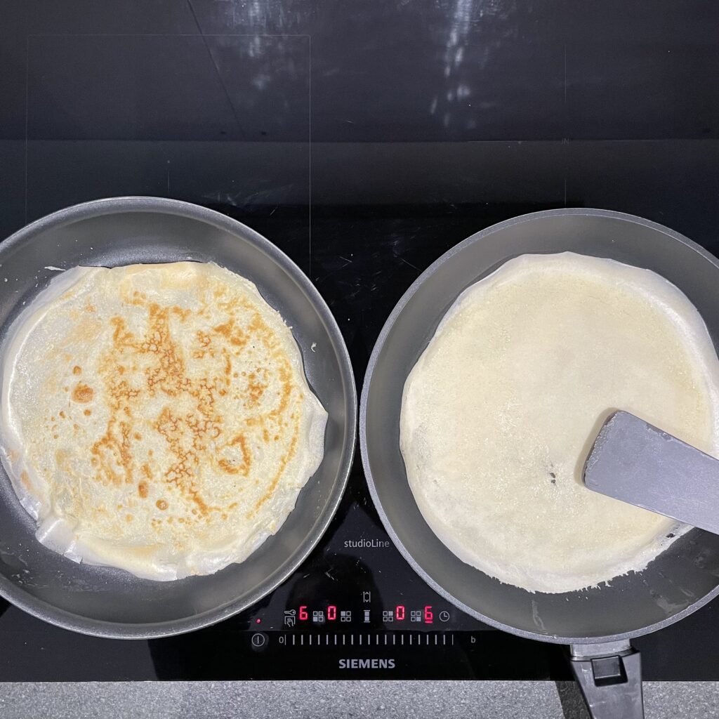 Two frying pans with pancakes in the making