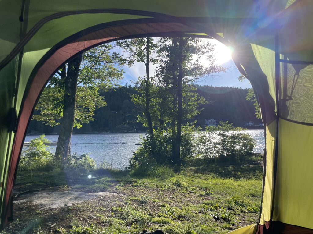 Photo from inside a tent showing a stunning view of trees and the sea on a sunny evening