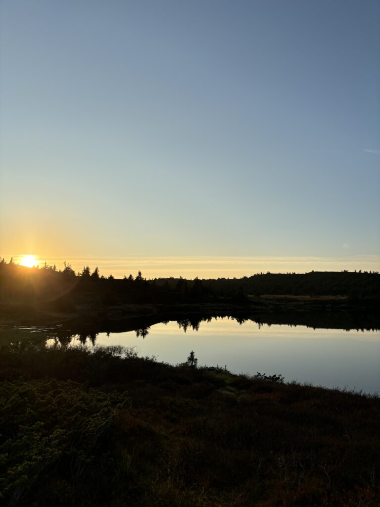 Photo of the sun setting over a small mountain lake.