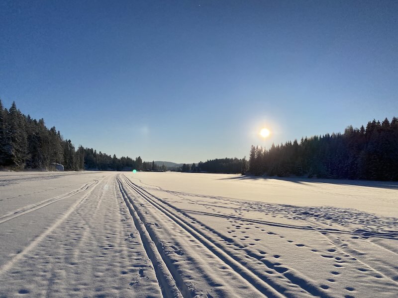 Photo taken on an ice covered lake, where snow covered skiing track are shown under a blue, sunny sky.